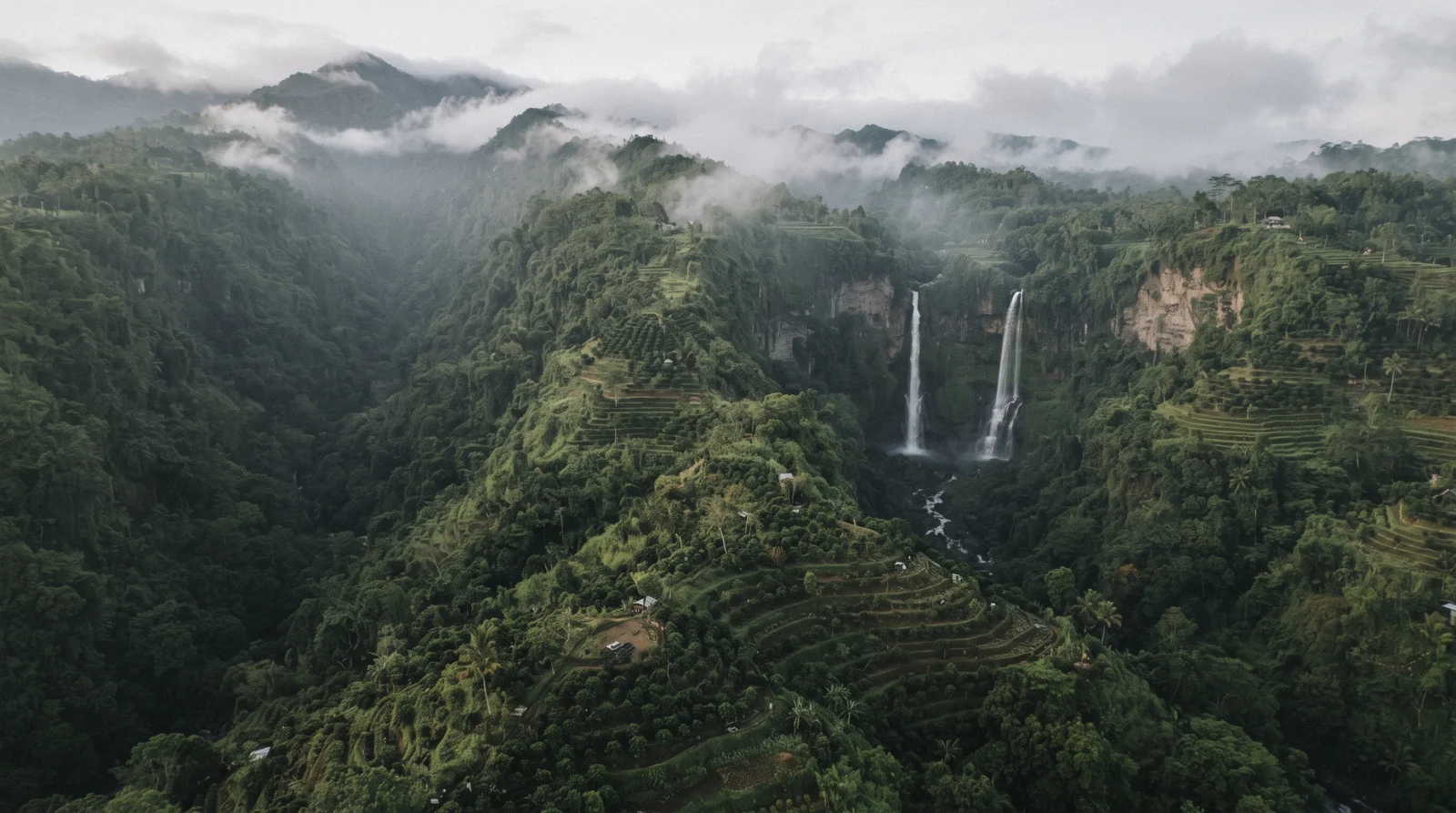 A tall multi-stream cascade pouring over a moss-covered cliff into a dark jungle pool, with wet stone steps and palms in the foreground, bali waterfalls in North Bali