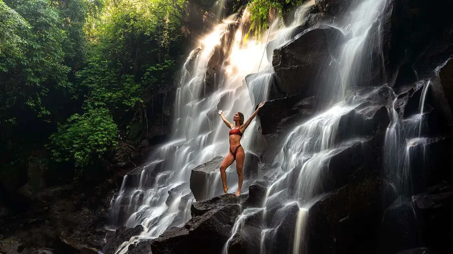Visitor standing on the tiered black rock ledges at Kanto Lampo Waterfall near Ubud Bali, the most photographed spot on the Ubud waterfall tours