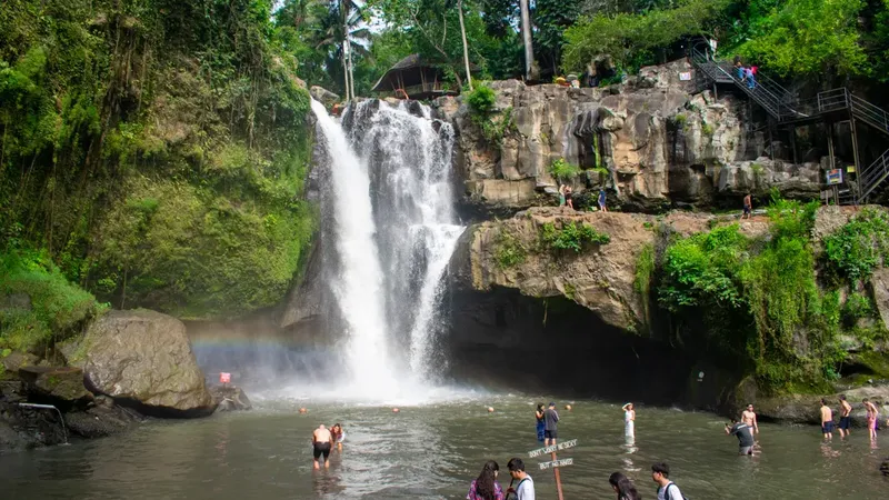 Small group of tourists standing at the base of Tegenungan Waterfall in Ubud Bali surrounded by lush jungle on a waterfall and temple day tour